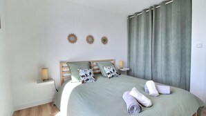 A neatly made bed with a green bedspread, two patterned pillows, and rolled towels on the side. There are three wall-mounted decorative mirrors and a bedside table with a lamp. - Maison 6 Personnes, SPA (Penmarc'h)