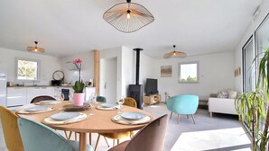 A modern kitchen with white cabinets, a dining area with a round table, and a living area with a sofa and a TV. - Maison 6 Personnes, SPA (Penmarc'h)