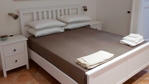 A bedroom with a white bed, two white nightstands, a white drawer, a brown mattress, and a purple wall art piece. - Carmine's Balcony (Napoli)