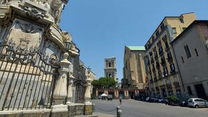 A cobblestone street with a historic building featuring ornate sculptures and a church in the background. - Carmine's Balcony (Napoli)