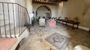 Un interior espacioso con suelo de piedra, techo de madera y escalera con barandilla de hierro forjado.