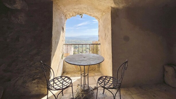 Un arco de piedra rústico que conduce a un balcón con una mesa y dos sillas, con vistas a un paisaje lejano.