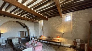 Una habitación rústica con paredes de piedra, vigas de madera, suelo de piedra, sofá rosa, mesa de madera y una lámpara.