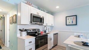 Una cocina moderna con armarios blancos, electrodomésticos de acero inoxidable y un cartel en la pared.
