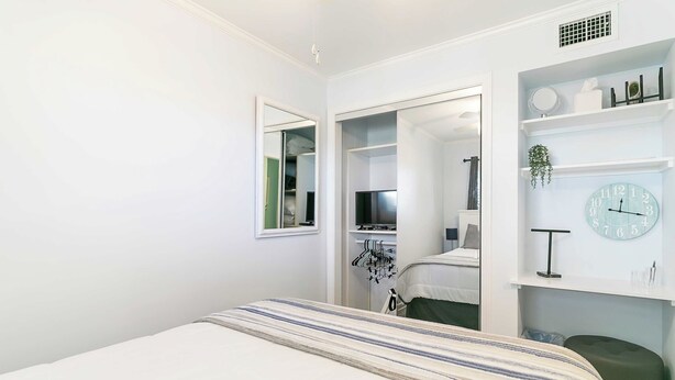 Un dormitorio con cama, armario, espejo, reloj y estante con varios objetos.