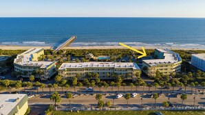 Un hotel frente al mar con vistas a la playa, varios estacionamientos y un muelle destacada que se extiende al océano.