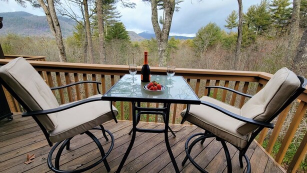 A wooden deck with a glass table and two chairs, a bottle of wine, and a glass of water. - Sapphire Mountain View Escape: Resort Amenities, Family & Pet Friendly! (Sapphire)