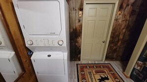 Un área de lavandería con lavadoras y secadoras apiladas, una puerta de madera y una alfombra estampada.