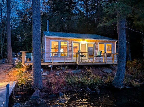 Una cabaña con terraza, ventanas amplias y un pequeño espacio exterior con un cartel.
