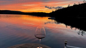 Un muelle de madera con una copa de vino tinto y vistas a un lago tranquilo al atardecer.