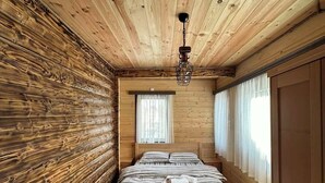 A wooden cabin bedroom with a bed, a hanging light fixture, and a large window. - Zagrad Homes in Zabljak (Razvršje)