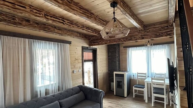 A living room with a sofa, a white coffee table, a fireplace, and a dining area with chairs and a table. - Zagrad Homes in Zabljak (Razvršje)