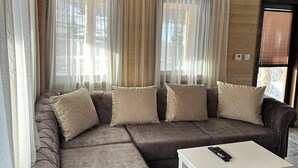 A modern living room with a sectional sofa, a white coffee table, and sheer curtains. - Zagrad Homes in Zabljak (Razvršje)