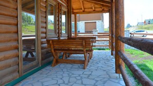 A wooden cabin with a covered patio, stone flooring, and a view of the surrounding landscape. - Zagrad Homes in Zabljak (Razvršje)