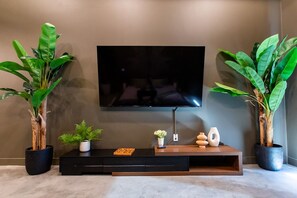 Un salon moderne avec un téléviseur à écran plat fixé au mur, un meuble de rangement noir en dessous, et deux grandes plantes en pot de chaque côté.