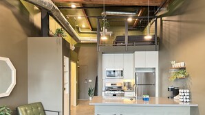Una cocina moderna con electrodomésticos de acero inoxidable, una isla central con taburetes de bar y una zona de estar con una butaca de cuero verde.