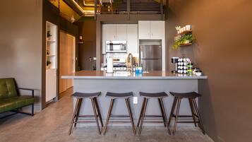 A modern kitchen with a central island, bar stools, and a green sofa.