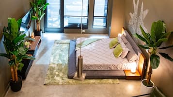 Une chambre à coucher moderne avec un lit, des tables de chevet, une grande fenêtre et des plantes en pot.