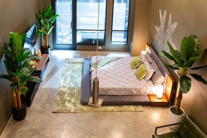 Ein modernes Schlafzimmer mit Bett, Nachttischen, einem großen Fenster und Topfpflanzen.