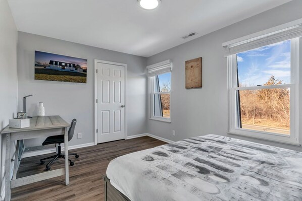 A bedroom with a bed, a desk, and a chair. There are two windows and a door.