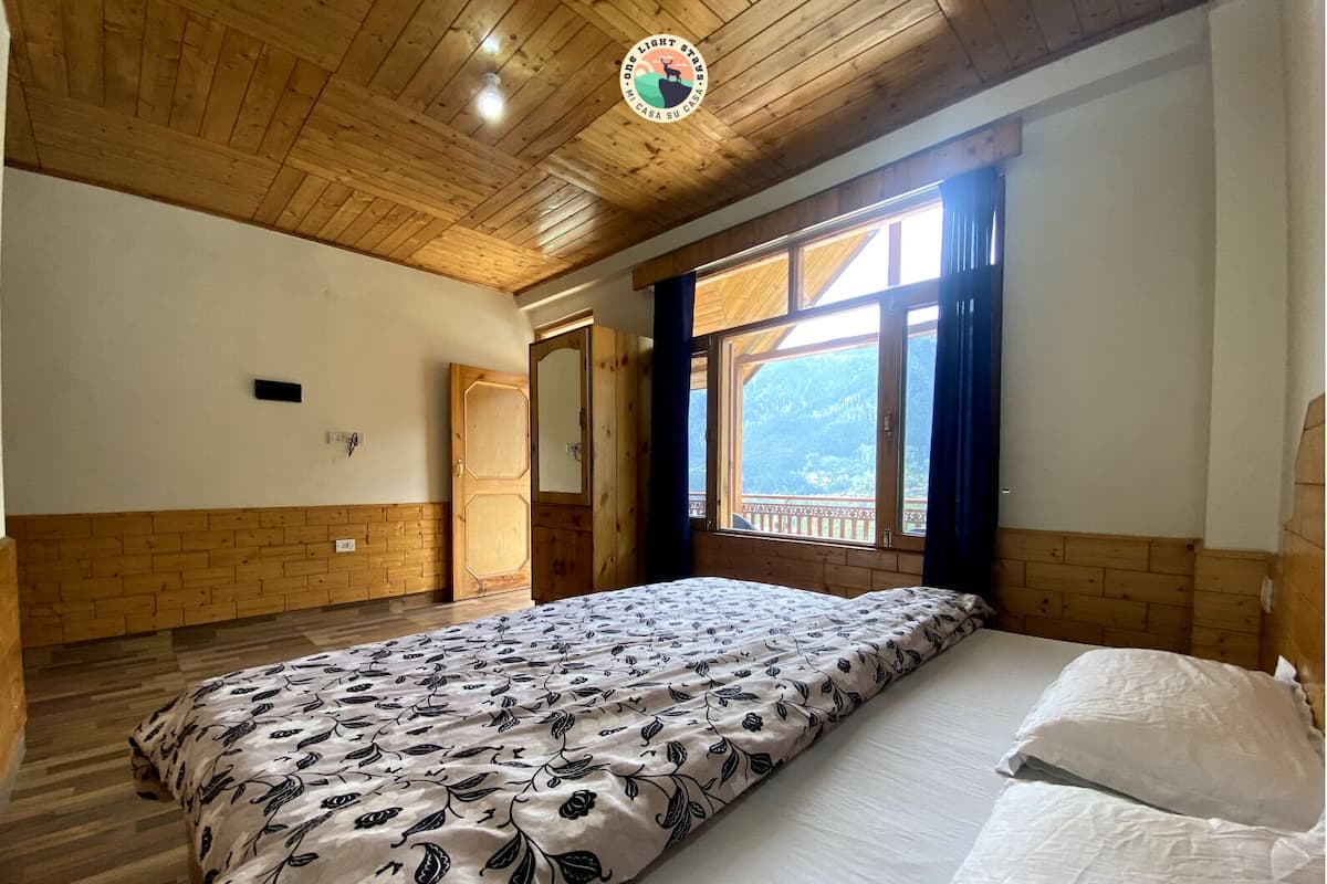 A bedroom with a wooden ceiling, a large bed with patterned bedding, a window with a view of mountains, and a door.