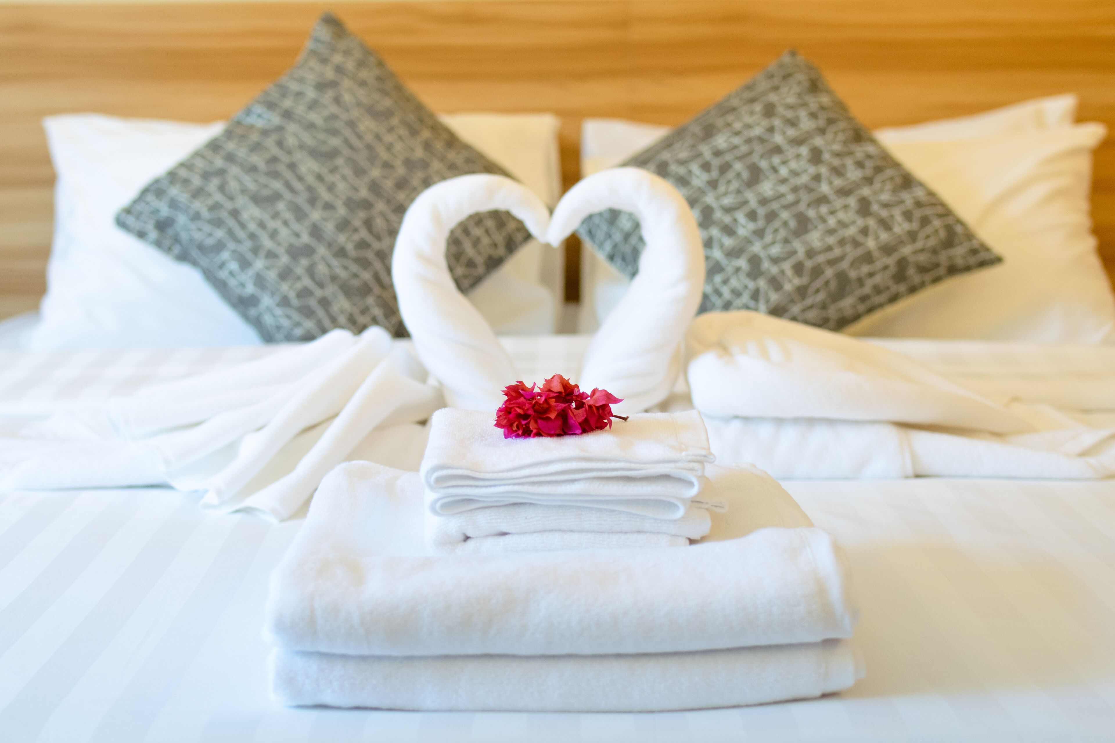 A neatly made bed with white towels folded in the center, a heart-shaped towel arrangement, and two patterned pillows.