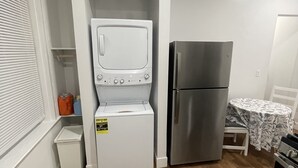 A compact kitchen with a built-in washer and dryer, a refrigerator, and a dining area with a table and chairs. - Home away from home, has all the amenities you need to have a comfortable stay. (Saint Bernard)