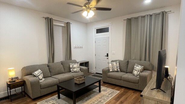 A modern living room with two sofas, a coffee table, a TV, and a ceiling fan. - Home away from home, has all the amenities you need to have a comfortable stay. (Saint Bernard)