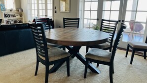 Un coin repas avec une table ronde en bois entourée de quatre chaises, un canapé en cuir foncé et une bibliothèque avec des photos encadrées.