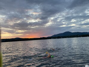 Nadador en un lago con una puesta de sol y montañas al fondo.
