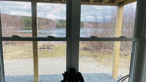 A room with a large window, wooden beams, and a small black object on the windowsill.