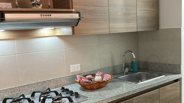 A modern kitchen with wooden cabinets, a gas stove, a built-in oven, and a stainless steel sink. - Hermoso Apartamento Mosquera (guayacan)
