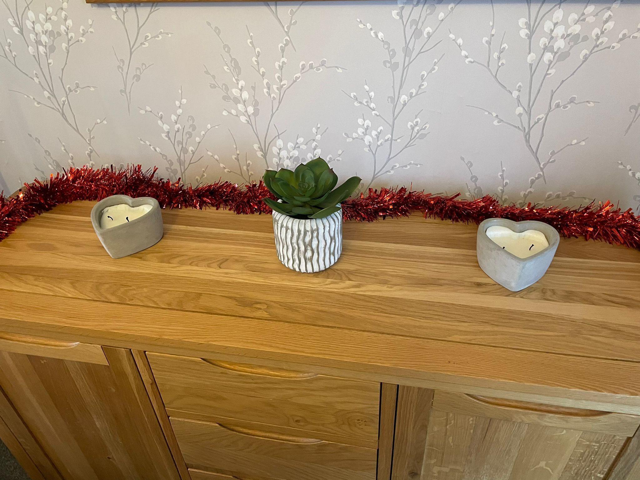 A wooden counter with three heart-shaped candle holders and a potted plant.