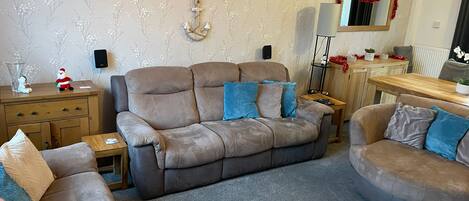 A living room with a beige sofa, a round armchair, a wooden side table, and a small table with a lamp.