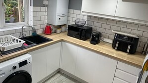 A compact kitchen with white cabinets, a washing machine, a microwave, a coffee maker, and a toaster. - Beautiful 3-bed House in Romford (Romford)