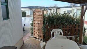 En udendørs terrasse med et rundt bord og stole, en træport og udsigt til nabohuse.
