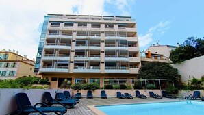 Un hotel de varios pisos con piscina, sillas de descanso y balcones.