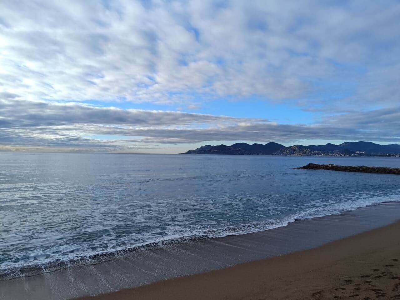 Una playa con un promontorio rocoso y montañas al fondo.