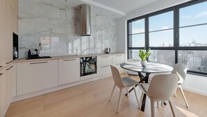 A modern kitchen with a marble backsplash, stainless steel range hood, and a dining area with a round table and chairs. - Doki -Montownia View by Grand Apartments (Gdansk)