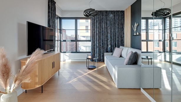 A modern living room with a large TV, a wooden cabinet, a white sofa, and large windows with curtains. - Doki -Montownia View by Grand Apartments (Gdansk)