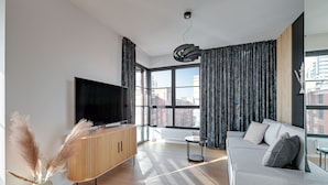 A modern living room with a flat-screen TV, a wooden cabinet, a grey sofa, and a small round table. - Doki -Montownia View by Grand Apartments (Gdansk)