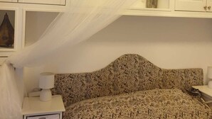 Un dormitorio con cama, mesita de noche, lámpara, jarrón decorativo y dosel.