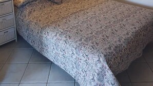 Un dormitorio con una colcha estampada con motivos florales, una mesita de noche con lámpara y un mueble de pared sobre la cama.