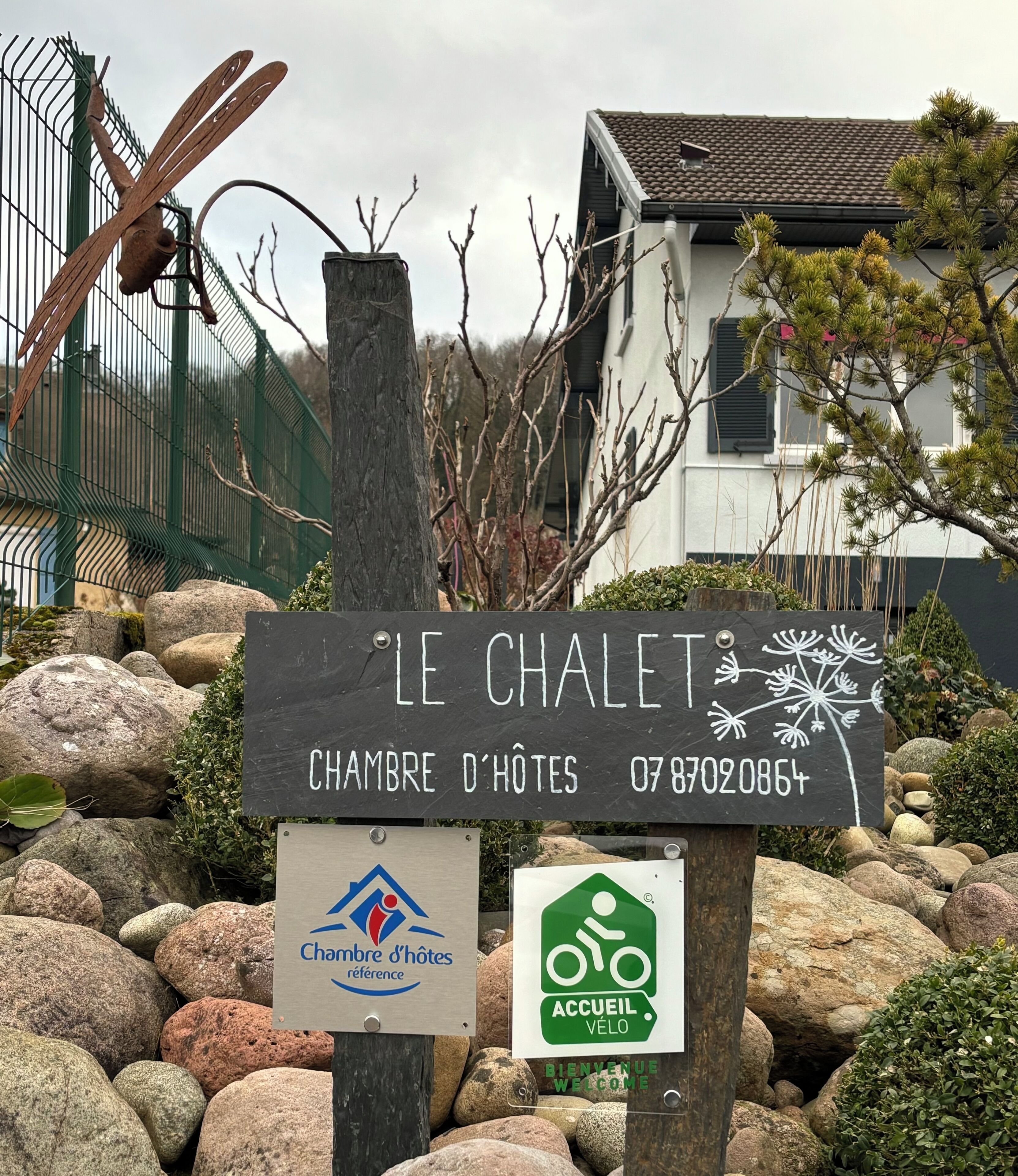 A sign for 'Le Chalet' with a contact number, a logo for 'Chambre d'hôtes', and a bicycle welcome sign.