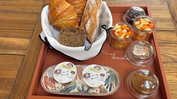 Un plateau contenant des croissants, du pain, de la compote de fruits, de la confiture, du fromage et du beurre.