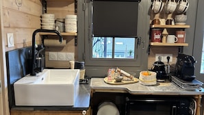 A compact kitchen with a sink, stove, and microwave. It features wooden cabinetry, a window with a view, and various kitchen utensils and appliances.