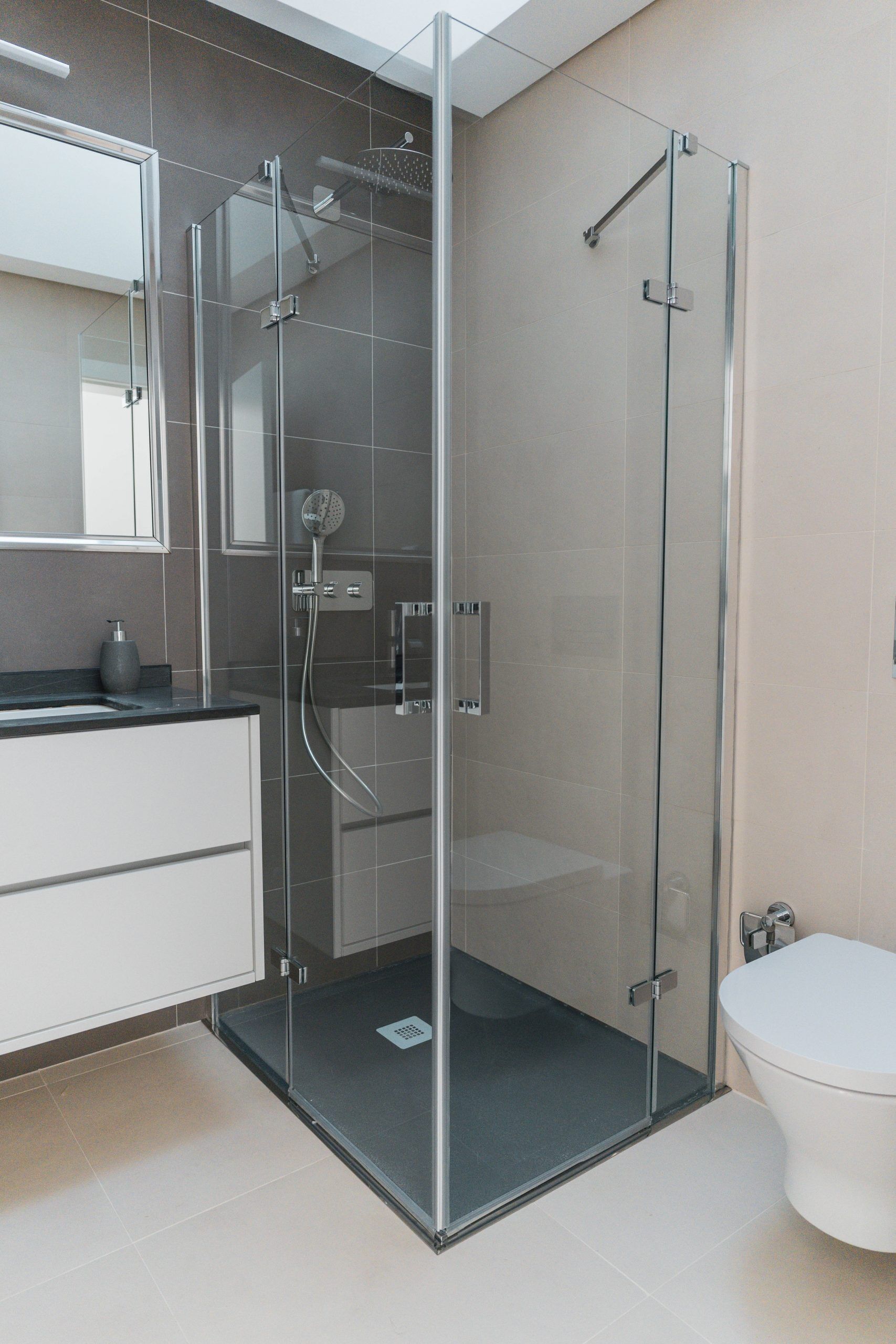 Un baño moderno con ducha envuelta en vidrio, inodoro blanco y tocador con espejo.
