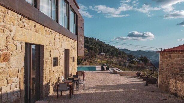 A stone building with a pool, outdoor seating, and a view of the mountains.