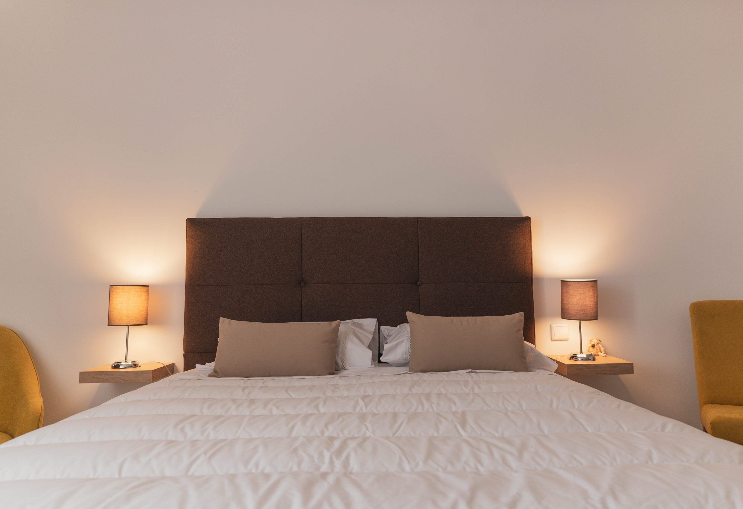 A neatly made bed with a headboard, two bedside lamps, and two chairs.
