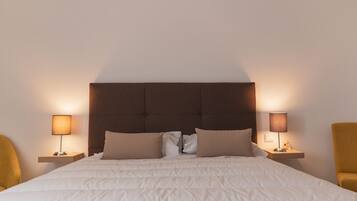 A neatly made bed with a headboard, two bedside lamps, and two chairs.
